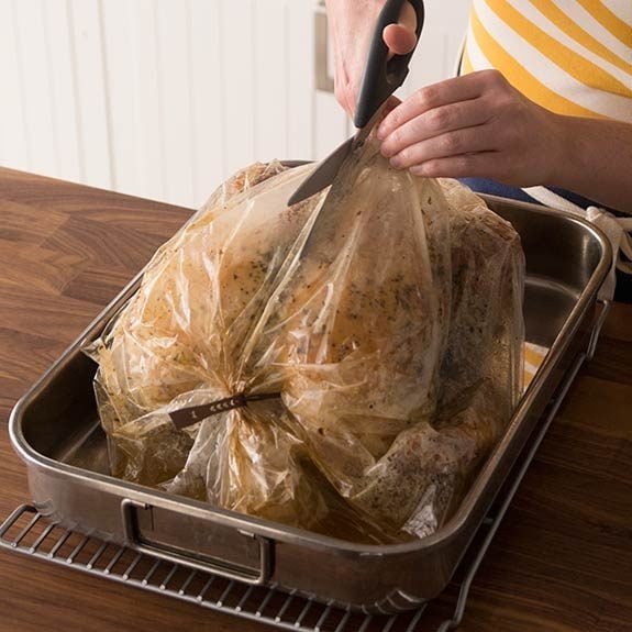Removing turkey in a roasting bag from the oven and cutting bag open.