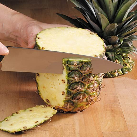 Alt=”Cutting a pineapple from the crown to the base.”