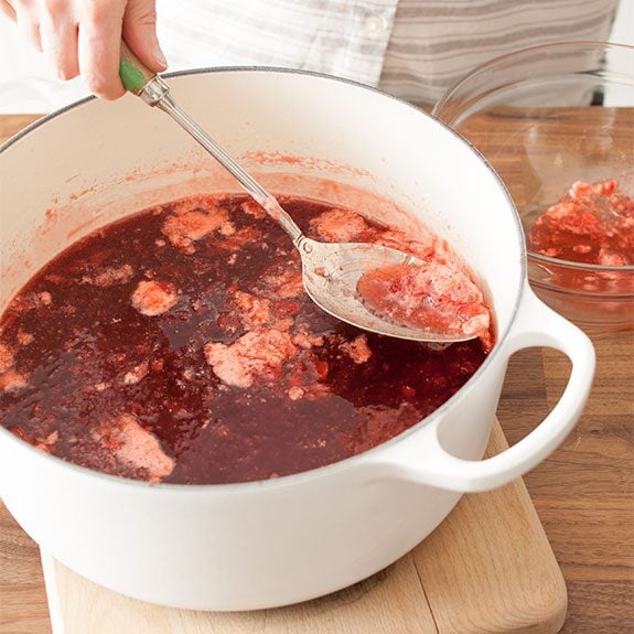 Skimming the foam off fresh strawberry jam with a big spoon